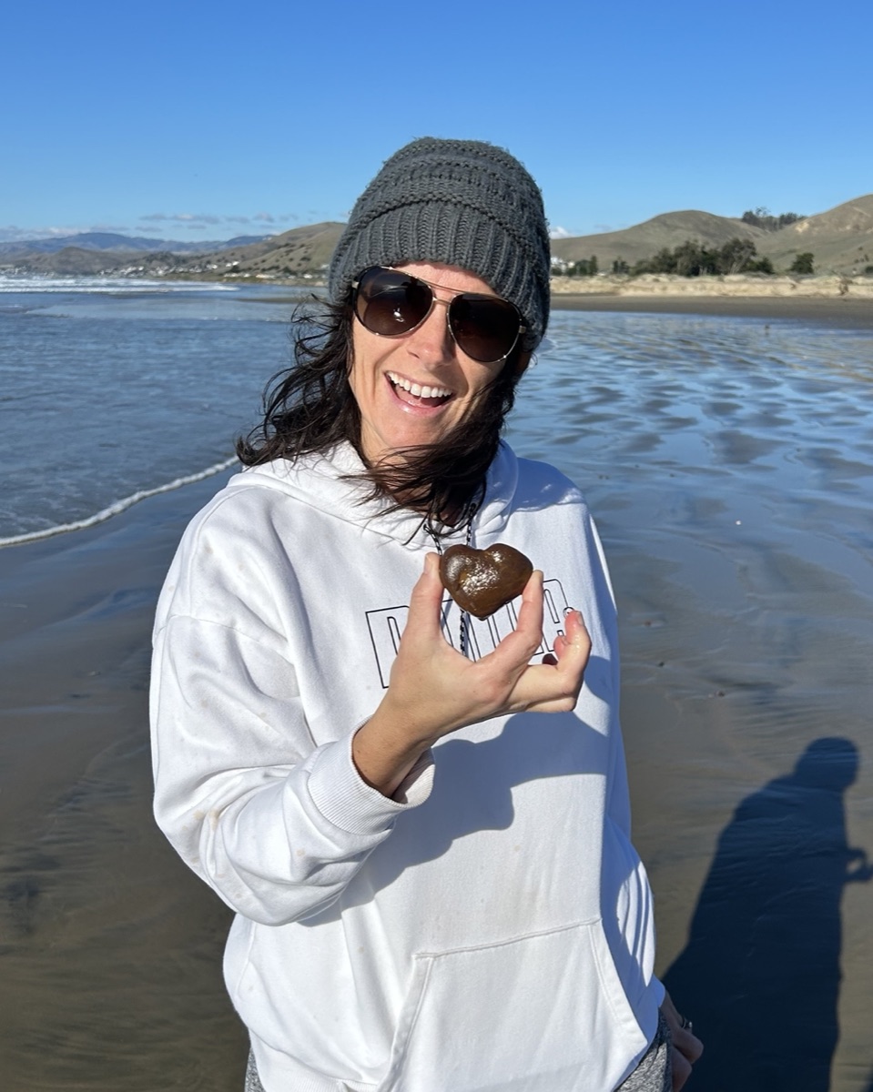 Erin holding a heart-shaped rock on the beach